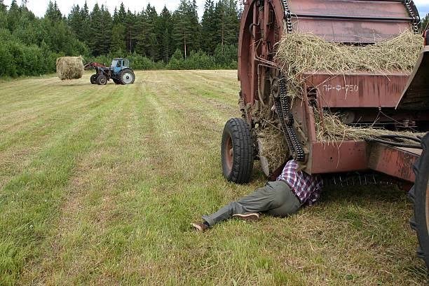 Mecânico fazendo manutenção em enfardadeira no campo com peças expostas, ilustrando parada na safra.