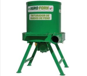 Triturador forrageiro processando feno em ambiente rural, com saída de material triturado, ilustrando a eficiência e robustez das máquinas da Agroforn no manejo alimentar do rebanho.