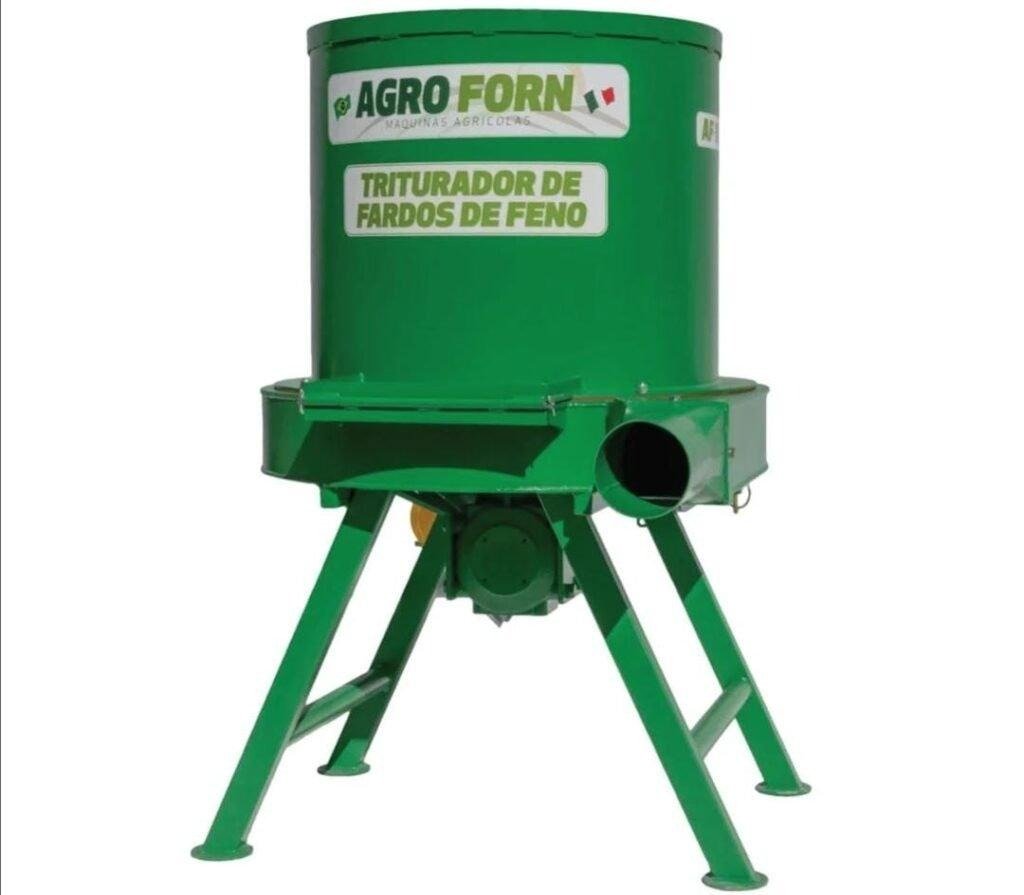 Triturador forrageiro processando feno em ambiente rural, com saída de material triturado, ilustrando a eficiência e robustez das máquinas da Agroforn no manejo alimentar do rebanho.