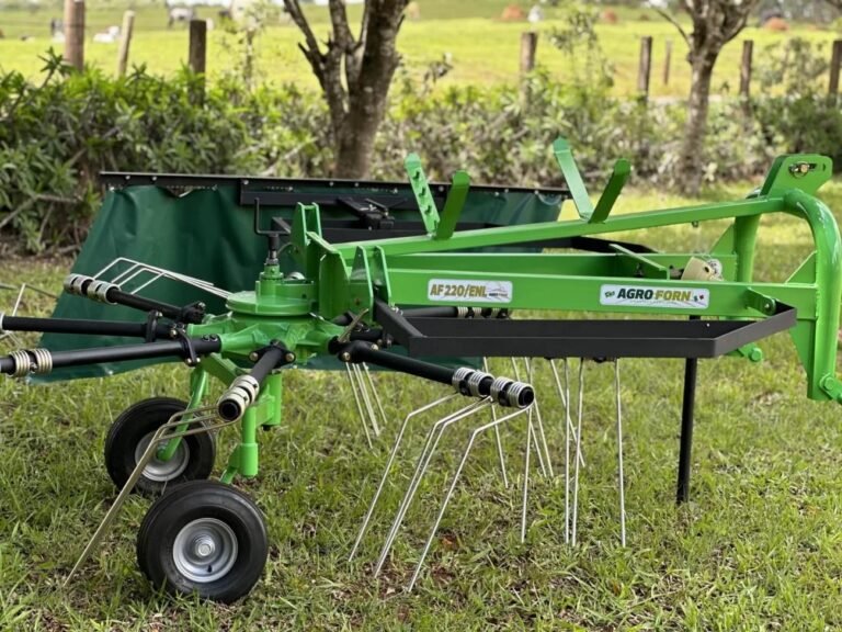 Ancinho enleirador AF320/8 da Agroforn acoplado ao trator formando leiras de feno no campo, com distribuição uniforme da forragem para facilitar o enfardamento.
