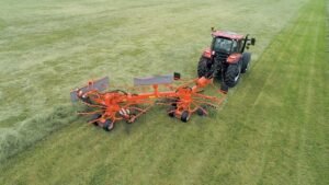 Enleirador para trator em operação no campo formando leiras uniformes de feno, destacando a eficiência dos equipamentos para fenação da Agroforn.